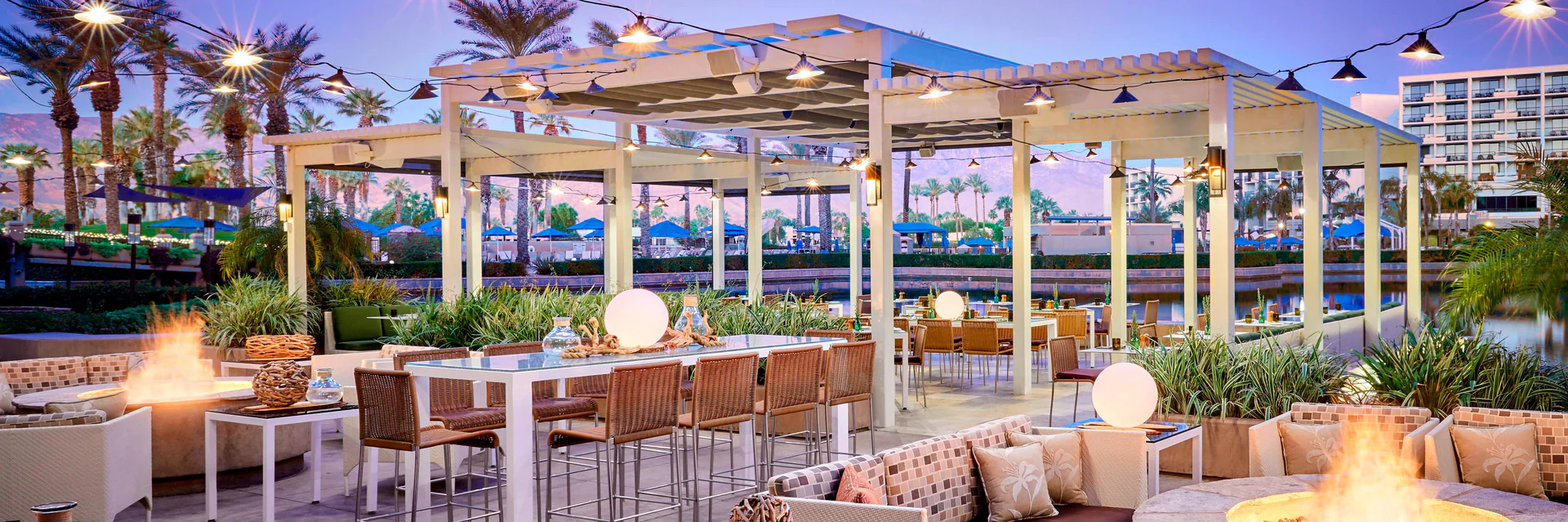 Poolside restaurant terrace under string lights with desert mountains behind it