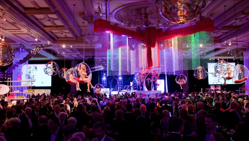 Black-tie gala ballroom with aerial performers and a packed crowd
